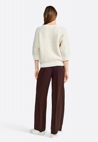 Maglione testurizzato beige chiaro con maniche a tre quarti, abbinato a pantaloni larghi marroni e scarpe slip-on grigio chiaro.