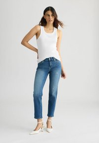 Valge ribaga T-särk, millel on peen logo, koos siniste sirgete lõikega denim teksadega, millel on kerge kulumine, ning valged kontsad.