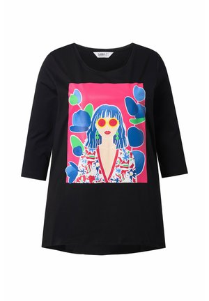 Sort t-shirt med et livligt grafisk motiv af en kvinde med blåt hår og røde solbriller på en lyserød baggrund, med blomsterdesign akcentuerer.