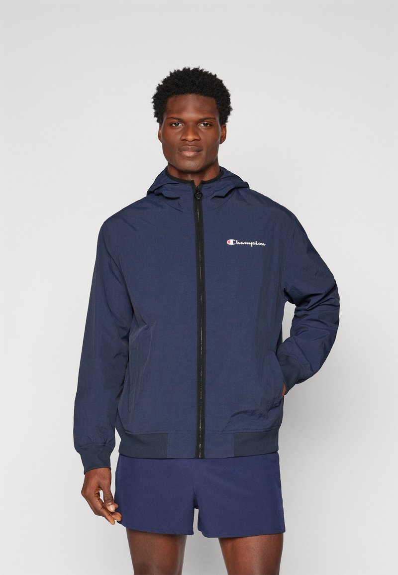 Navy hooded jacket made of lightweight material, featuring a front zipper and logo on the left chest. Smooth texture with elastic cuffs.
