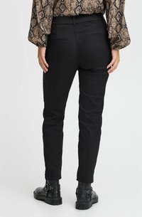 Juodos slim-fit kelnės su lygiu paviršiumi ir kišenėmis, derinamos su juodomis kulkšninių batais. Viršus turi gyvatės rašto dėlionę neutraliomis spalvomis.