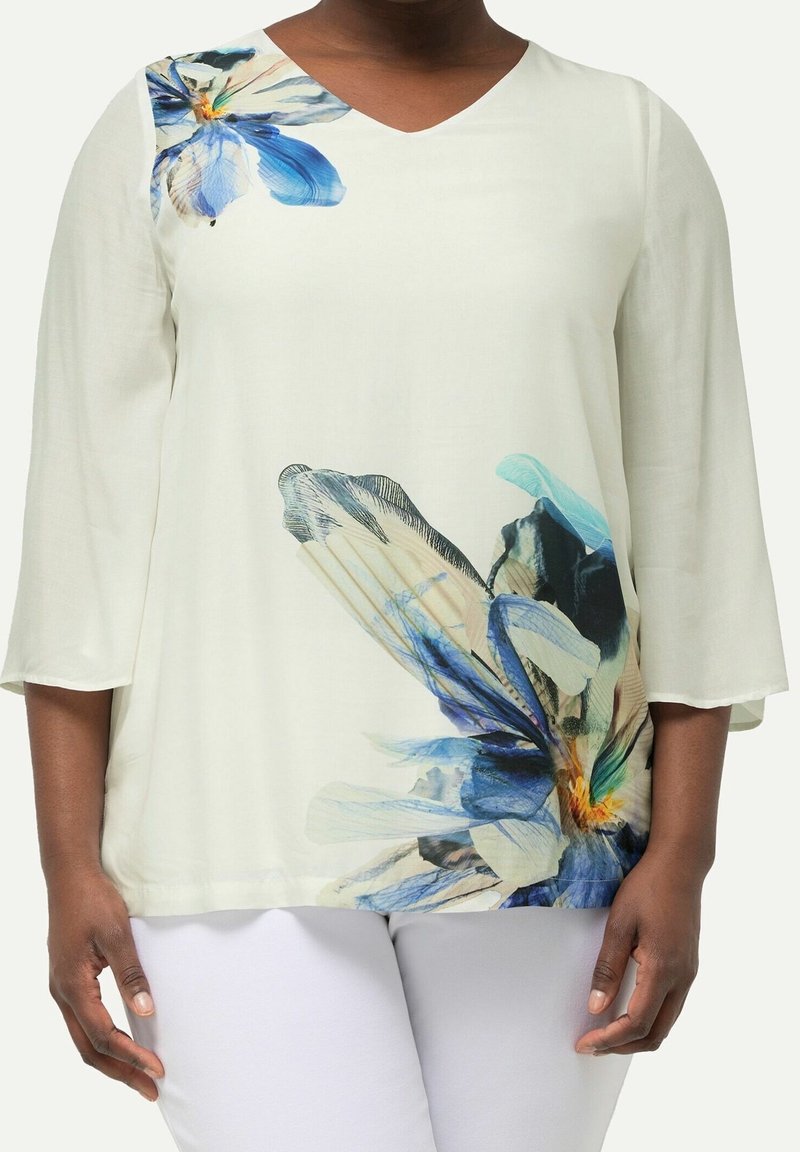Blusa bianca con stampa floreale colorata in blu e verde. Scollo a V, maniche a tre quarti e vestibilità ampia. Tessuto morbido.