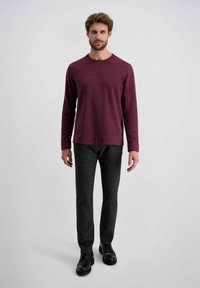 Bordeaux rood langarm shirt met een ronde hals, van een gestructureerde stof, gecombineerd met donkere broek en zwarte schoenen, weergegeven op een neutrale achtergrond.