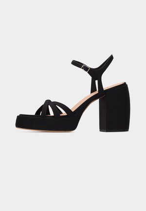 Μαύρο σανδάλι πλατφόρμα με χοντρό ψηλό τακούνι, τρεις μπροστινούς ιμάντες και ρυθμιζόμενο λουράκι αστραγάλου με ασημί πόρπη.