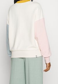 Sudadera blanca de cuello redondo con mangas en bloques de color azul, rosa y amarillo. Material suave, corte relajado y puños acanalados. Pequeño detalle de logo en el dobladillo.