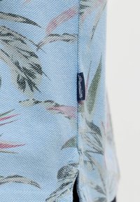 Tissu bleu clair avec un motif floral et une petite étiquette bleu marine portant la mention « Premium » cousue dans une couture latérale.