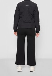 Svart vadderad jacka med rund krage och logotyp på baksidan, matchad med svarta vida byxor och ljusa skor.