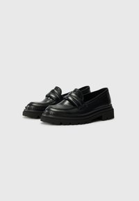 Black leather loafers with a thick rubber sole, featuring a stitched design and a broad strap across the instep. Smooth texture, rounded shape.