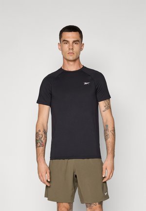 T-shirt de sport noire à manches courtes, col rond et logo Reebok sur la poitrine. Associé à un short vert olive. Texture de tissu lisse.