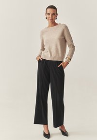 Beżowy sweter z dzianiny z okrągłym dekoltem i długimi rękawami, zestawiony z czarnymi szerokimi spodniami. Czarne buty na wysokim obcasie oraz złota bransoleta mankietowa.