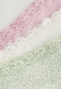 Kanten versieringen in roze, wit en groen geplaatst boven een textiel met een structuur van stippen in lichtgroen en blauw. Fijne bloemenkant details.