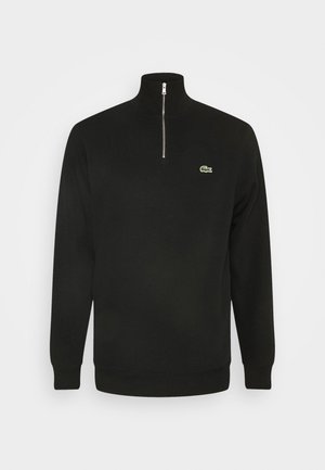 Svart zip-neck sweatshirt laget av mykt stoff. Har en grønn logo på venstre bryst, ribbede mansjetter og høyt kragedesign.
