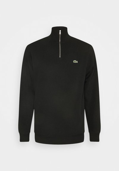 Sweat-shirt à col zippé noir, fabriqué en tissu doux. Présente un logo vert sur la poitrine gauche, des poignets côtelés et un design de col haut.