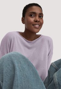 Hellpurpurfarbener, langärmeliger Pullover mit weitem Ausschnitt, kombiniert mit lockeren blauen Jeans. Geschmeidige Textur, lässige Passform, entspannter Look.