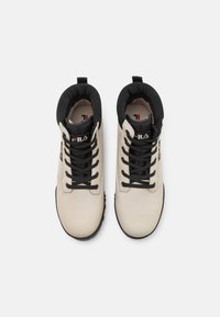 Stivali da trekking beige con accenti neri, lacci robusti, colletto imbottito, interno testurizzato e suola in gomma per trazione. Logo Fila presente.
