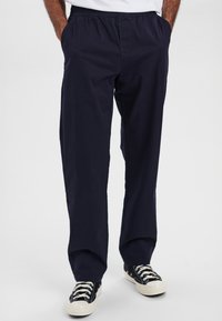 Marineblå bomuldsbukser med elastisk talje, sidelommer og afslappet pasform, parret med sort-hvide sneakers.