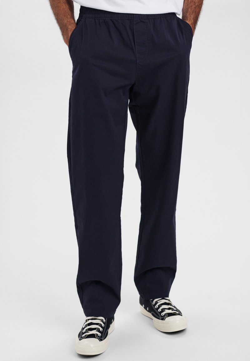 Marineblå bomuldsbukser med elastisk talje, sidelommer og afslappet pasform, parret med sort-hvide sneakers.