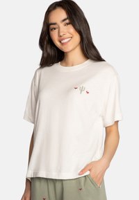 T-shirt bianca in cotone con maniche corte, caratterizzata da un ricamo di un cactus verde e un cuore rosso sul petto. Vestibilità rilassata e texture liscia.