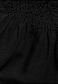 Tissu noir avec des détails smockés en haut, d'une texture douce et d'un léger éclat, créant des plis et un mouvement délicat.
