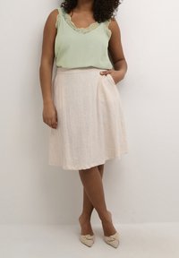 Light green sleeveless top with lace trim, paired with a knee-length cream skirt featuring pockets. Beige pointed flats complete the outfit.