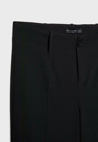 Pantalon noir taille haute cintré avec passants de ceinture, fermeture avant par bouton, et étiquette de marque Stradivarius à l'intérieur de la ceinture.