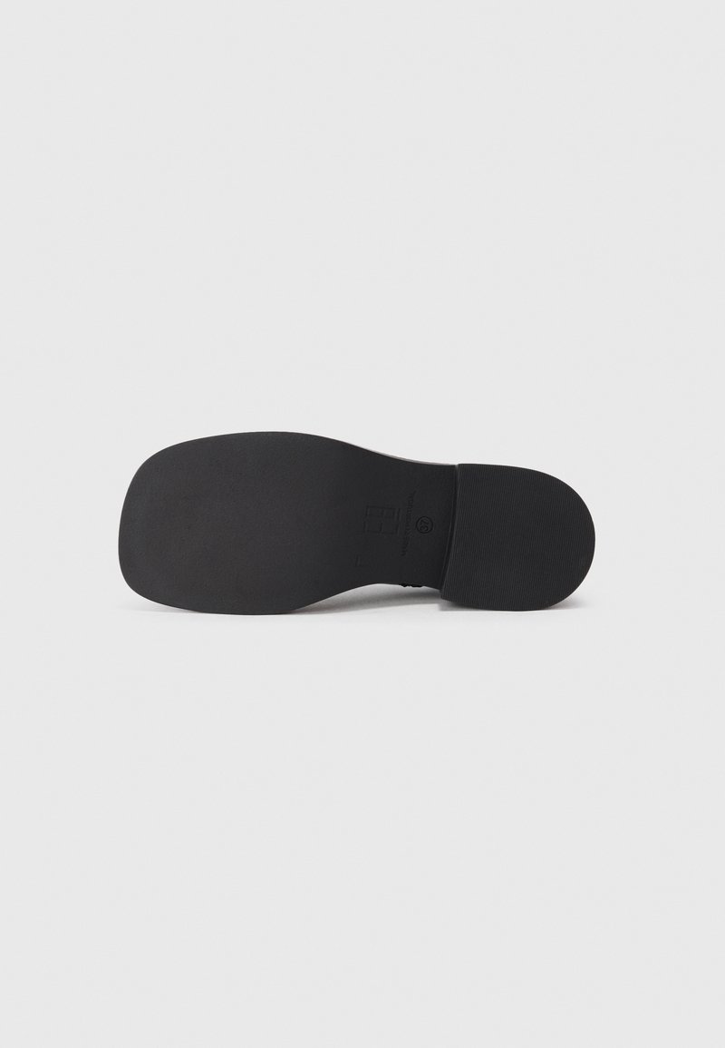 Suola di scarpa nera con una finitura liscia, motivo di grip leggermente strutturato, punta arrotondata e branding minimale impressa nell'area del tallone.