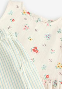 Detské šaty krémovej farby s malými kvetinovými a srdcovými vzormi, doplnené o svetlomodré a biele pásikavé nohavice s elastickým pásom.
