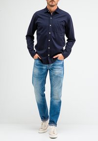 Navyblauw button-up overhemd met een borstzak, gecombineerd met vervaagde lichtblauwe jeans en beige sneakers. Het overhemd heeft een kraag ontwerp.