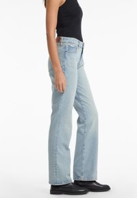 Heledsinised denim püksid, millel on lahtine istuvus, sirged sääred, viie tasku disain ja klassikaline vöökoht, kombineerituna mustade pahkluu saapatega.