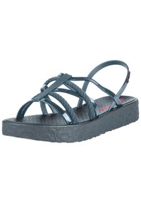 Blue platform sandals with crisscrossed straps, made from rubber and textured material, featuring a low sole and adjustable heel strap.