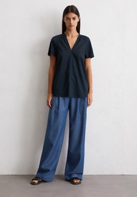 Navy short-sleeve blouse with a v-neck, paired with wide blue denim trousers and black slide sandals, featuring a relaxed fit and smooth texture.