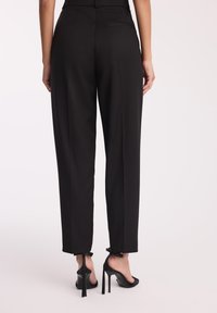 Czarne spodnie o prostym kroju, z tylną kieszenią i wiązaniami na kostkach. W połączeniu z czarnymi szpilkami.