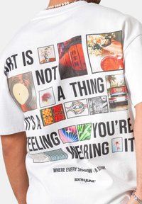 Persona que lleva una camiseta blanca con cuadrados coloridos que muestran flores, un disco, un coche y un texto que dice "El arte no es una cosa, es un sentimiento que llevas puesto."