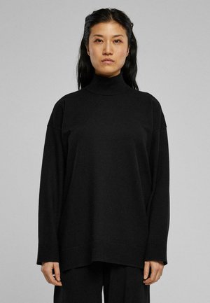 Schwarzer Rollkragenpullover mit langen Ärmeln, oversized Schnitt und geripptem Saum. Glatte Textur mit einer lockeren Silhouette. Getragen mit passenden Hosen.