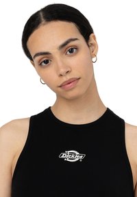 Top sans manches noir en tissu lisse, avec un logo "Dickies" blanc sur la poitrine et un col rond. Design simple et ajusté.