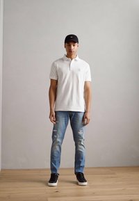 Hvid polo shirt, slidte lyseblå jeans og sorte sneakers. Simpelt design; ensfarvede farver; kasket fuldender det afslappede look.