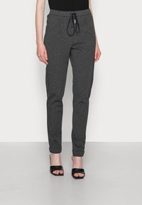 Šedé kostkované tepláky s šňůrkou v pase a elastickými manžetami. Materiál je lehký a má texturovaný vzor. Design s plochým předním dílem.