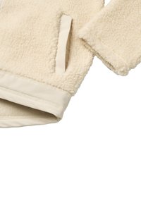 Manica e bordo della tasca di una giacca in pile color crema con bordo in tessuto liscio su sfondo bianco.