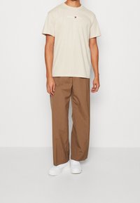 Beige bavlněné tričko s logem "Tommy Jeans", spárované s hnědými skládacími kalhotami a bílými teniskami. Jednoduchý design a uvolněný střih.