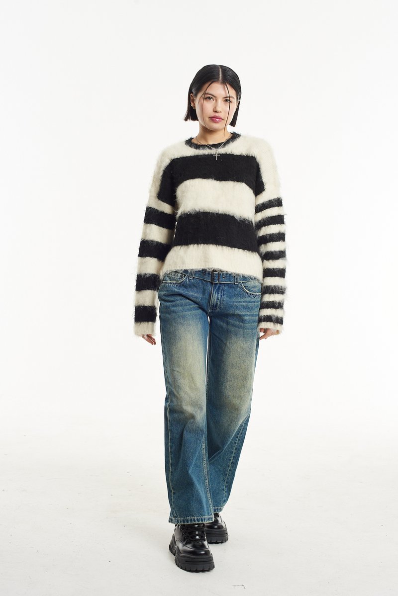 Črno in kremo črtast pulover s puhasto teksturo, v kombinaciji s bledimi modrimi širokimi hlačami in debelimi črnimi čevlji.