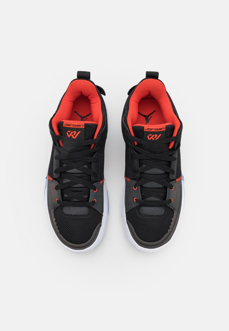 Chaussures de sport noires et grises avec tige en maille, accents rouges, lacets plats, col rembourré et semelle blanche ; présente un logo sur la languette.