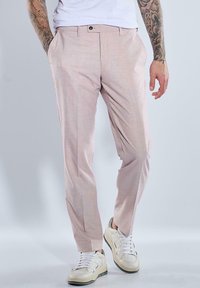 Helle rosa maßgeschneiderte Hose aus strukturierter Stoff; hat einen flachen Bund und seitliche Taschen, kombiniert mit weißen Sneakers.