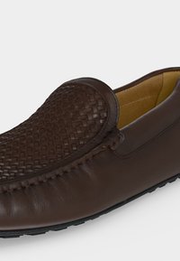 Καφέ δερμάτινο loafer με υφαντή λεπτομέρεια στο πάνω μέρος και ραμμένα άκρα, με επενδεδυμένη ταμπά εσωτερική επένδυση και μαύρη λαστιχένια σόλα.