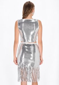 Silbernes zweiteiliges Outfit mit einem bauchfreien Top und einem Fransensaum-Rock, auffallend durch seine glänzende, mit Pailletten besetzte Textur und eine figurbetonte Passform.