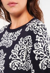 Granatowy sweter z białym wzorem kwiatowym, dzianinowa tekstura, okrągły dekolt i ściągacz. Szczegółowe hafty na ramieniu.