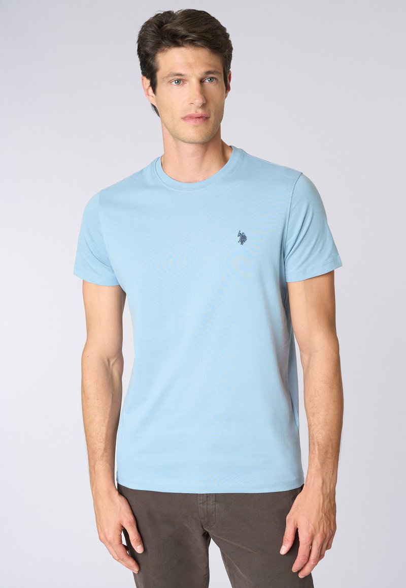 T-shirt in cotone azzurro chiaro con maniche corte e scollatura rotonda. Presenta un piccolo logo scuro sulla parte sinistra del petto. Texture liscia.