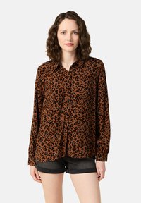 Brun leopardmönstrad skjorta med knappar, lång ärm och krage, kombinerad med mörka shorts. Slät textur och avslappnad passform.