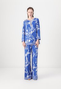 Blauw gemusterd twee-delig outfit met een lange mouw top met een ronde hals en broek met wijde pijpen, beiden versierd met witte abstracte ontwerpen.