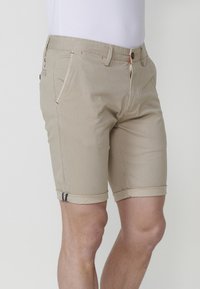 Beige shorts made of textured fabric, featuring rolled cuffs, front pockets, and contrasting stitching accents. Button and zipper closure.