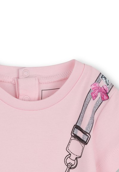 Różowy bawełniany T-shirt z okrągłym dekoltem i zatrzaskami, z nadrukiem szarych szelek ozdobionym różową kokardką na ramieniu.